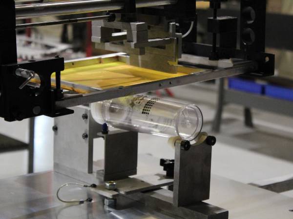 A machine is screen printing patterns on the glass bottle.